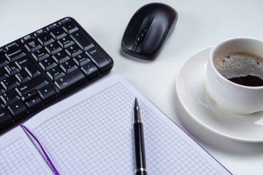 Ofis tablo Masası. Çalışma alanı boş not defteri, klavye, ofis malzemeleri ve beyaz arka plan üzerinde kahve fincanı.