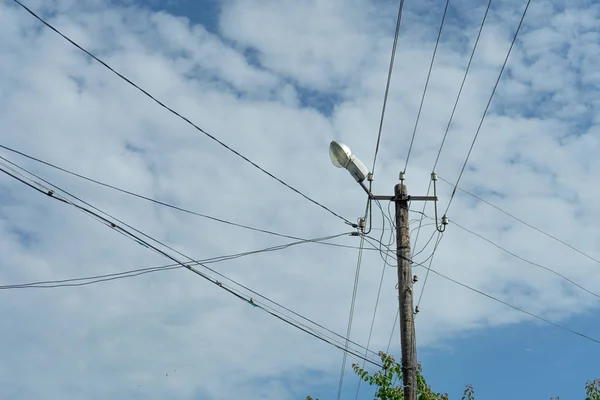 Stary drewniany słup elektryczny z lampą i wieloma kablami, które działają w różnych kierunkach, Chmura Niebo. — Zdjęcie stockowe