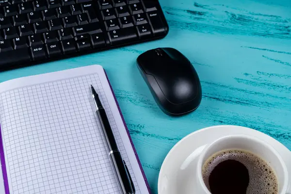 Escritorio de mesa de oficina. Espacio de trabajo con libreta de notas, teclado, útiles de oficina y taza de café sobre fondo de madera . — Foto de Stock