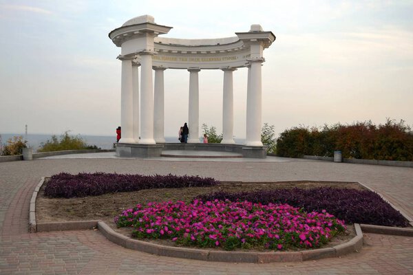 White gazebo in Poltava (Ukraine) with beautiful columns, in front of which a bright flowerbed of purple autumn flowers