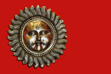 Kırmızı zeminüzerinde yüzü ve bıyığı olan bronz güneş. Surya.