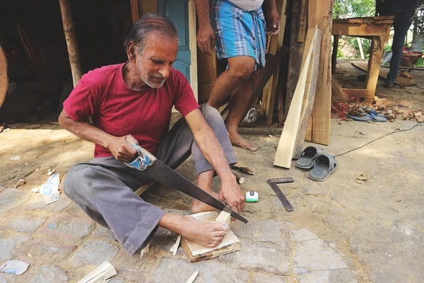 stock image Elderly Indian man working on wood. An Indian citizen carpenter sawing a wooden object with a hand saw. India, Mayapur, March 19, 2019.