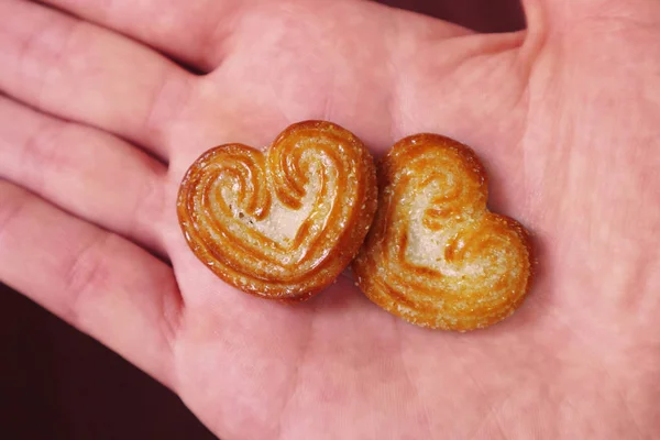 Two heart-shaped cookies lie on the palm. A young caucasian man holds two hearts in his hand.