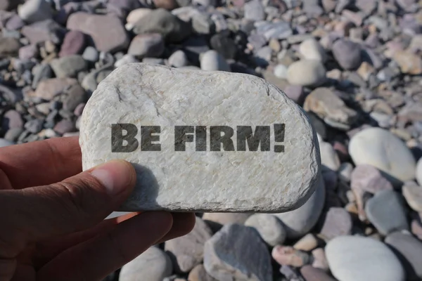 hand holding rock with be firm! lettering in bright sunlight