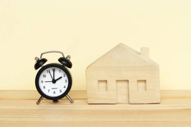 sarı arka plan ile ahşap masa üzerinde çalar saat ve küçük ev