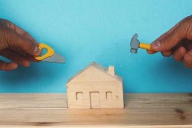 küçük ahşap kulübe ve el tutan oyuncak testere ve çekiç, onarım konsepti