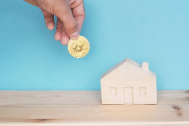 el tutan bitcoin sikke ve mavi arka plan üzerinde küçük ahşap ev