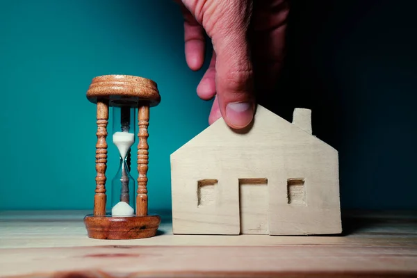 テーブルの上に砂時計と小さな木造の家を保持する手 — ストック写真