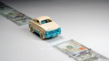 mavi arka planda oyuncak araba ve dolar banknotları.