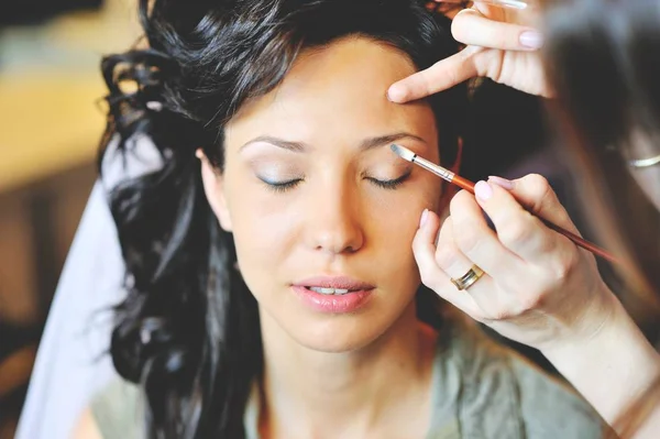 Jovem noiva bonita aplicando maquiagem de casamento por artista de maquiagem — Fotografia de Stock