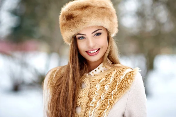 雪の冬の公園で毛皮の帽子の笑顔とカメラを見て幸せな美しい笑顔の女性の肖像画 — ストック写真