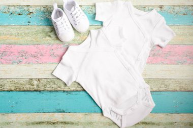 Beyaz bebek onesie ve pastel ahşap arka plan üzerinde spor ayakkabısı. Aferin tasarımınızı yerleştirin. Yukarı alay.