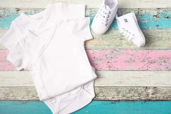 Beyaz bebek onesie ve pastel ahşap arka plan üzerinde spor ayakkabısı. Aferin tasarımınızı yerleştirin. Yukarı alay.