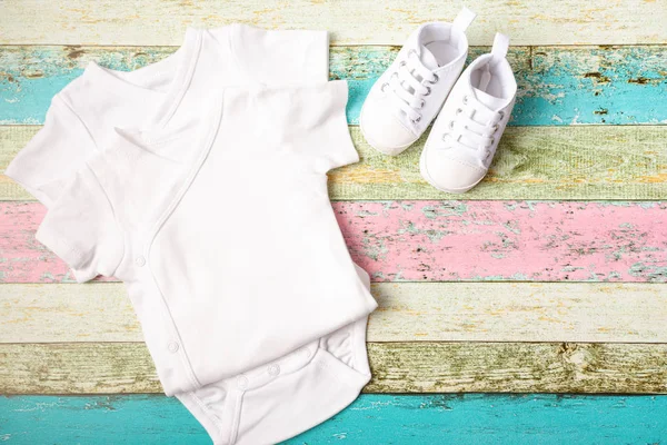 Beyaz bebek onesie ve pastel ahşap arka plan üzerinde spor ayakkabısı. Aferin tasarımınızı yerleştirin. Yukarı alay.