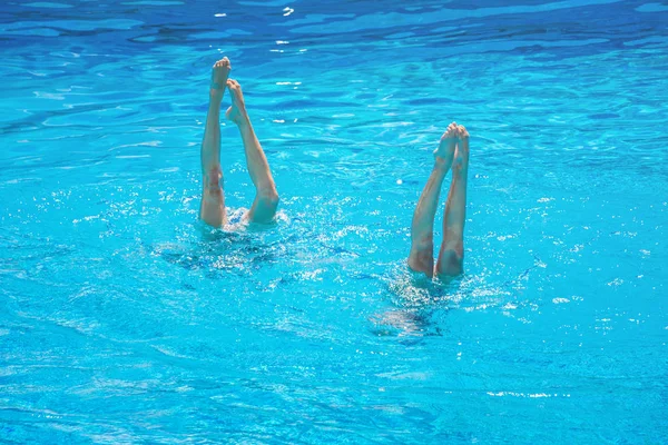 Synkroniserad simning. Vackra lean kvinnliga ben i vattnet i en pool. Begreppet skönhet, artisteri, atletiska och synkronicitet. — Stockfoto