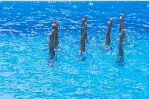 Natação sincronizada. Pernas femininas magras bonitas na água de uma piscina. Conceito de beleza, arte, atletismo e sincronicidade . — Fotografia de Stock