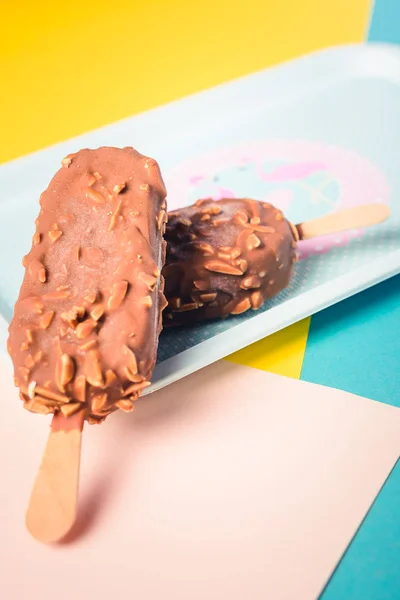 Десерт шоколадное мороженое с орехами, деревянная палочка на синем и желтом пастельном фоне. Эскимосы в синем винтажном подносе с розовыми фламингосандрами и точками. Летнее искушение. Крытый крупный план . — стоковое фото
