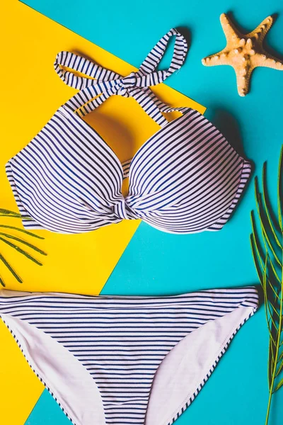 Vue de dessus de deux pièces maillot de bain rayé bleu et blanc sur fond pastel bleu et jaune. Concept de vacances . — Photo