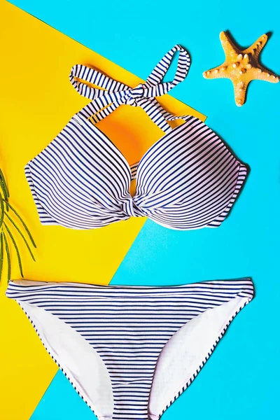 Vue de dessus de deux pièces maillot de bain rayé bleu et blanc sur fond pastel bleu et jaune. Concept de vacances . — Photo