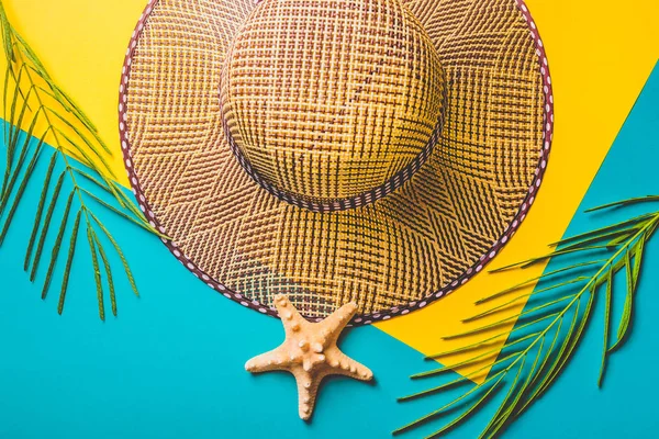 Composition estivale. Feuilles de palmier tropical, chapeau de plage en paille, étoile de mer sur fond bleu pastel et jaune. Concept voyage d'été. Pose plate, vue du dessus, espace de copie . — Photo