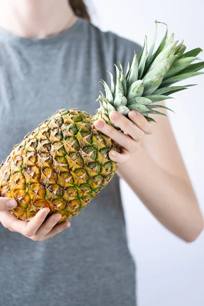 Girl holding a pineapple in hands on white background. Tropical, vacantion and summer vibes. Minimalist photoshot.