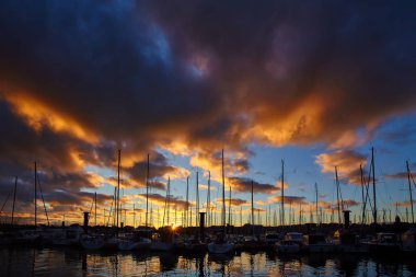 Bir sürü gündoğumu, iskelede uzun boylu gemi direkleri ile Yatlar