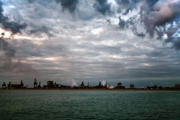 Oil refinery on the beach in the early gloomy morning. From the pipe of the plant smoke polluting the atmosphere.