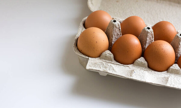 Pack of farm chicken eggs in cardboard container on white. Top view.