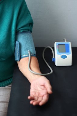 Yaşlı kadın ile bir masada oturan bir dijital tansiyon aleti, basınç ölçme