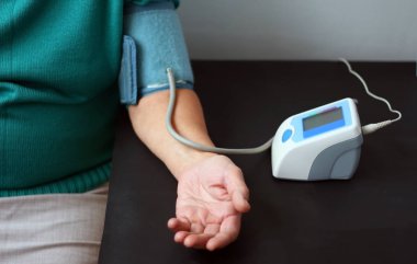 Yaşlı kadın ile bir masada oturan bir dijital tansiyon aleti, basınç ölçme