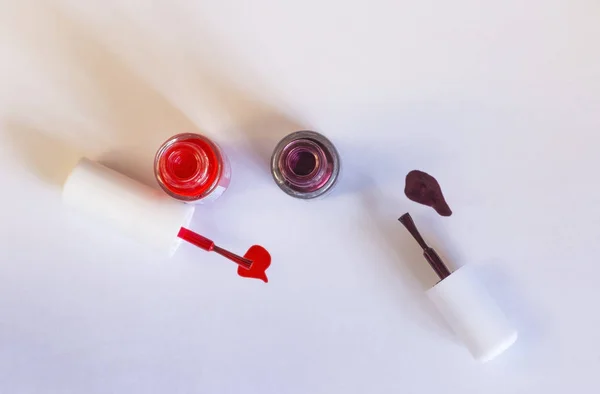 Bottles of colorful nail polish with their brushes displayed against a white background. Top view.