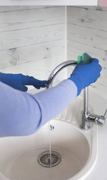 家庭主妇用蓝色橡胶手套清洁厨房水龙头 — 图库照片