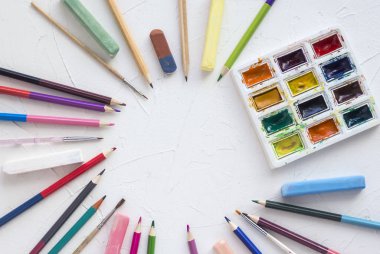 Suluboya boya çizim ve kurşun kalemler, fırçalarla tebeşir beyaz bir masaya. Herkesdaire oluşturacak şekilde düzenlenmiş