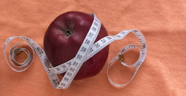 O conceito de uma dieta com uma maçã e fita métrica, em uma tela de fundo laranja com uma cópia do espaço — Fotografia de Stock