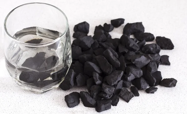 Piedras de shungita en un vaso para la purificación y recarga de agua — Foto de Stock