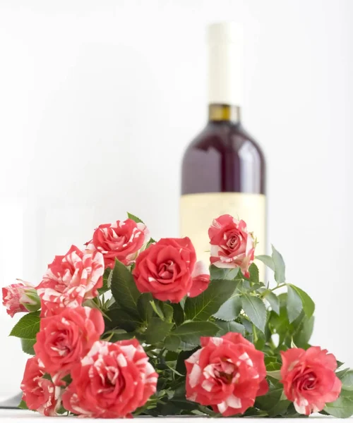 Красные пятнистые розы на белом фоне с бутылкой вина на заднем плане с копировальным пространством — стоковое фото