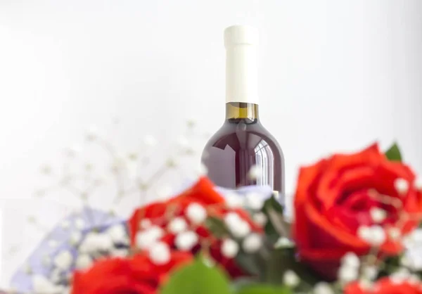 Uma garrafa de vinho com rosas vermelhas desfocadas em primeiro plano — Fotografia de Stock
