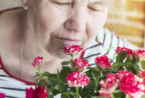 Een aangename bejaarde vrouw verheugt op de rozen en ademt hun aroma — Stockfoto