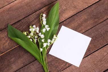 metin için beyaz kağıt bir levha ile kahverengi ahşap bir arka plan üzerinde yeşil yaprakları ile vadinin narin beyaz zambaklar