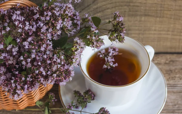 Egy csésze forró aromás tea oregánó gyógynövények egy kosárban egy fából készült háttér — Stock Fotó