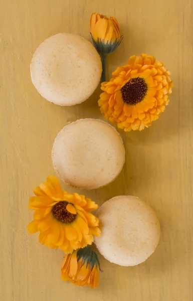 three delicate yellow almond cakes macaroons on a yellow background with calendula flowers .the view from the top