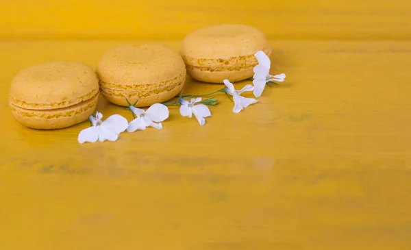 Yellow macaroons cake on yellow background with white flowers and copy space — Stock Photo, Image
