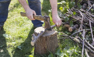 Elinde balta olan bir adam, kütüğün dallarını kesiyor.