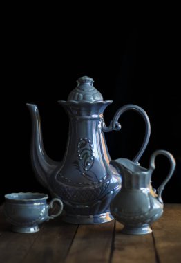 Bir çaydanlık, bir sütçü ve siyah arka planda bir kupadan oluşan mavi bir kahve setiyle hayat.