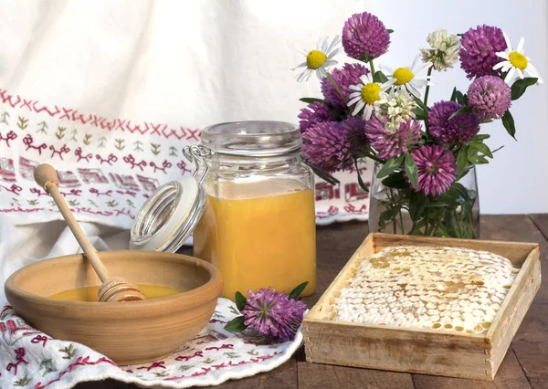 Μέλι σε βάζο και κύπελλο και κηρήθρα με κουτάλι μελιού και φόντο από λευκό ύφασμα και μπουκέτο αγριολούλουδα — Φωτογραφία Αρχείου