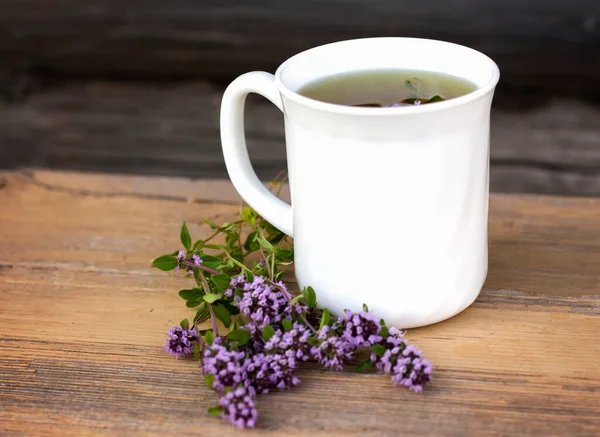 a white Cup of herbal tea with a bunch of fresh wild thyme on an old wooden background.