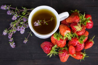 kekikli yeşil çay ve ahşap arka planda bir sürü kırmızı çilek..