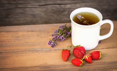 Çilek ve çimlerle boyanmış ahşap arka planda bir bardak çay..