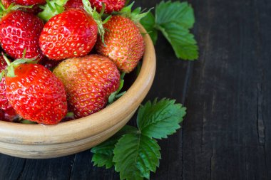 Bir fincan dolusu kırmızı sulu çilek siyah ahşap arka planda, üzerinde uzay kopyası olan yeşillikler..