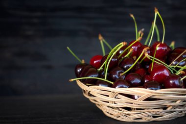 Karanlık, ahşap bir arka planda, hasır bir tabakta taze kiraz çilekleri ve uzay kopyası..